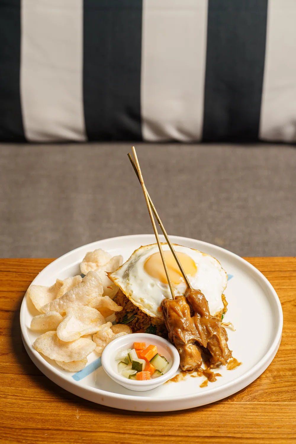 A rice dish served with a fried egg, satay skewers and crackers.