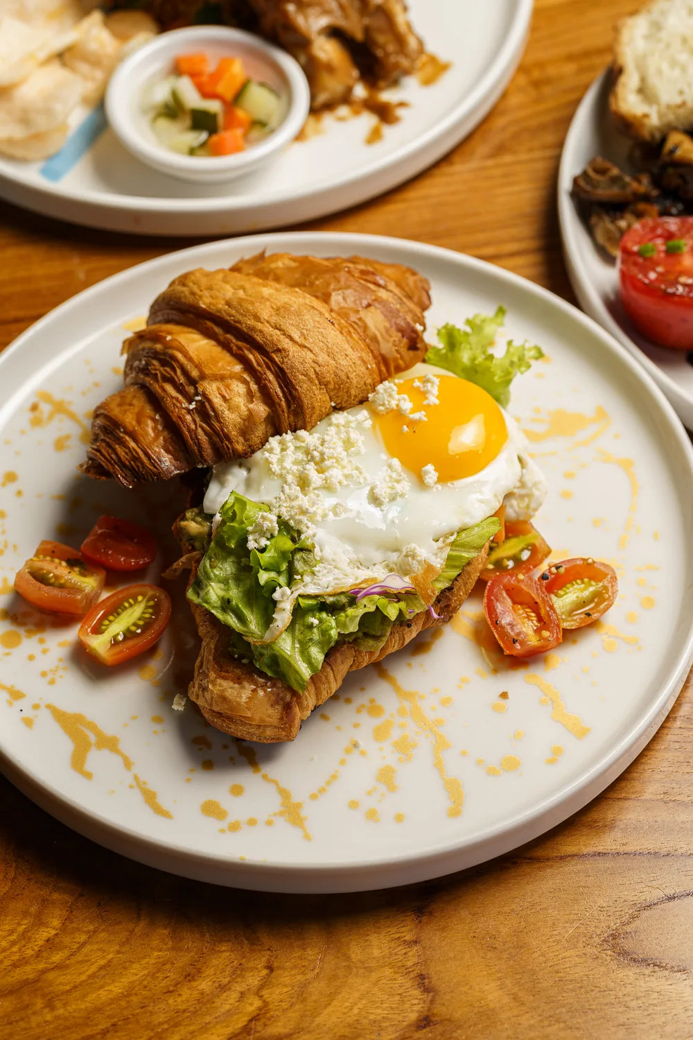 A croissant served with a fried egg, leafy greens and tomatoes.